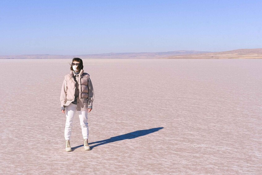 A person standing in a vast, flat, barren landscape with distant hills under a clear sky. 5