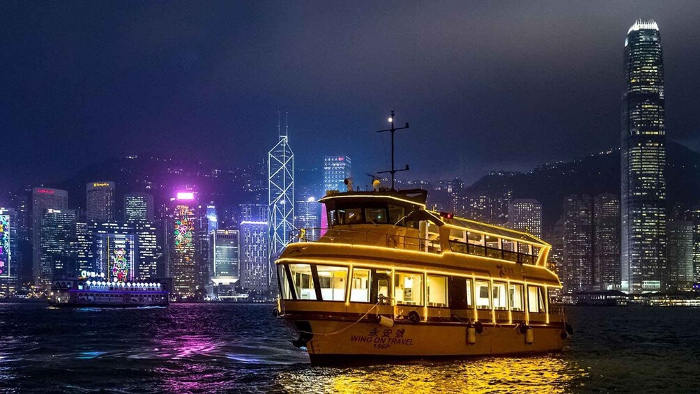 A brightly lit ferry boat with 'Wing on Travel' written on its side, sailing in a body of water with a city skyline in the background. 5