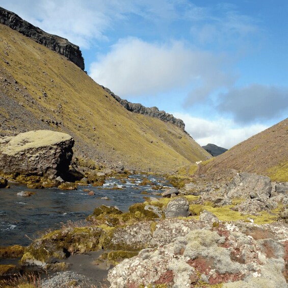 A mountain stream with rocky banks and a grassy hillside. 5