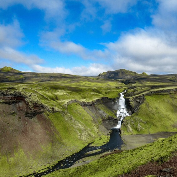 A waterfall in a green valley with mountains in the background. 3