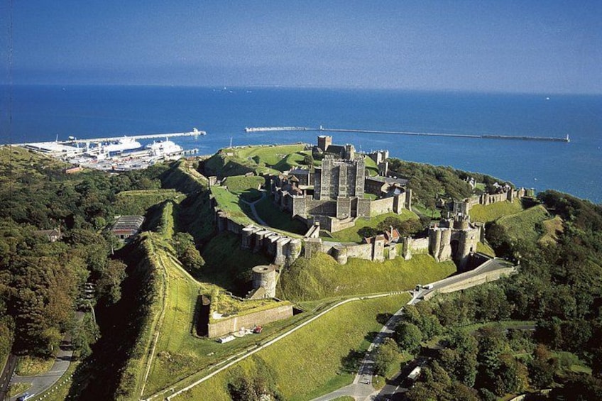 A historic castle surrounded by lush greenery and a coastal view. 1