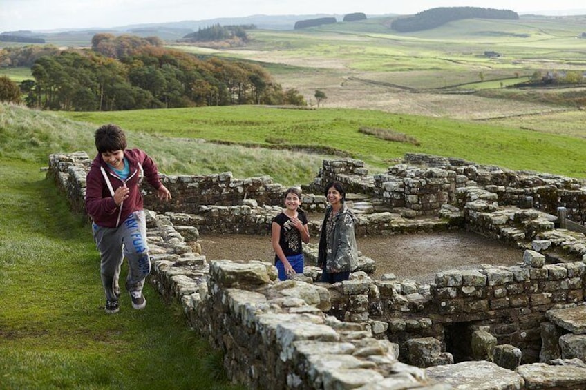 A historical stone structure with a grassy field and distant hills in the background. 1