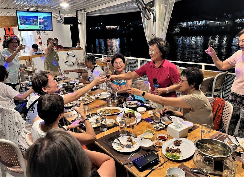 A group of people toasting at a dinner table on a boat with a cityscape in the background. 2