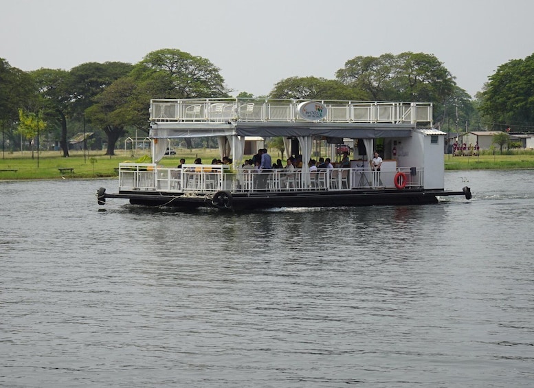 A riverboat with passengers, surrounded by trees and a grassy area. 1