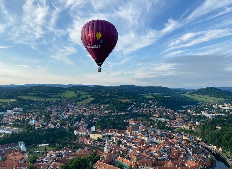 A hot air balloon over a town with a river and surrounding hills. 3