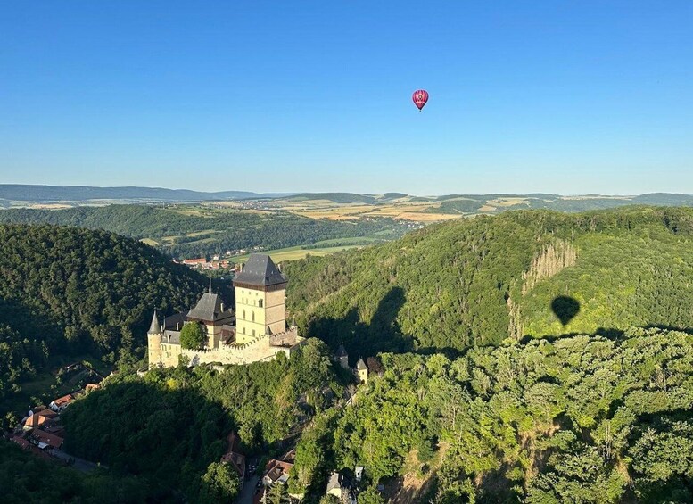 A castle surrounded by forested hills and a clear sky. 1