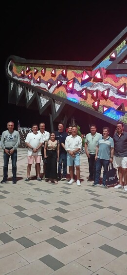 A group of people standing in front of a colorful, illuminated structure with geometric patterns. 2