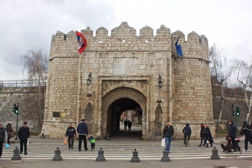 A stone castle entrance with flags, pedestrians, and traffic lights. 4