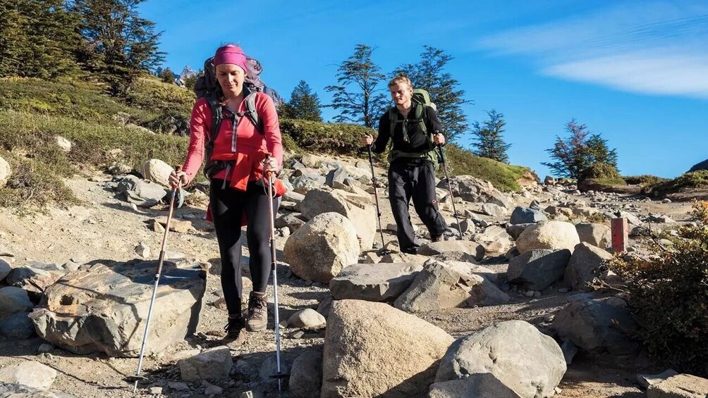 Two hikers on a rocky trail with large boulders and sparse vegetation. 5