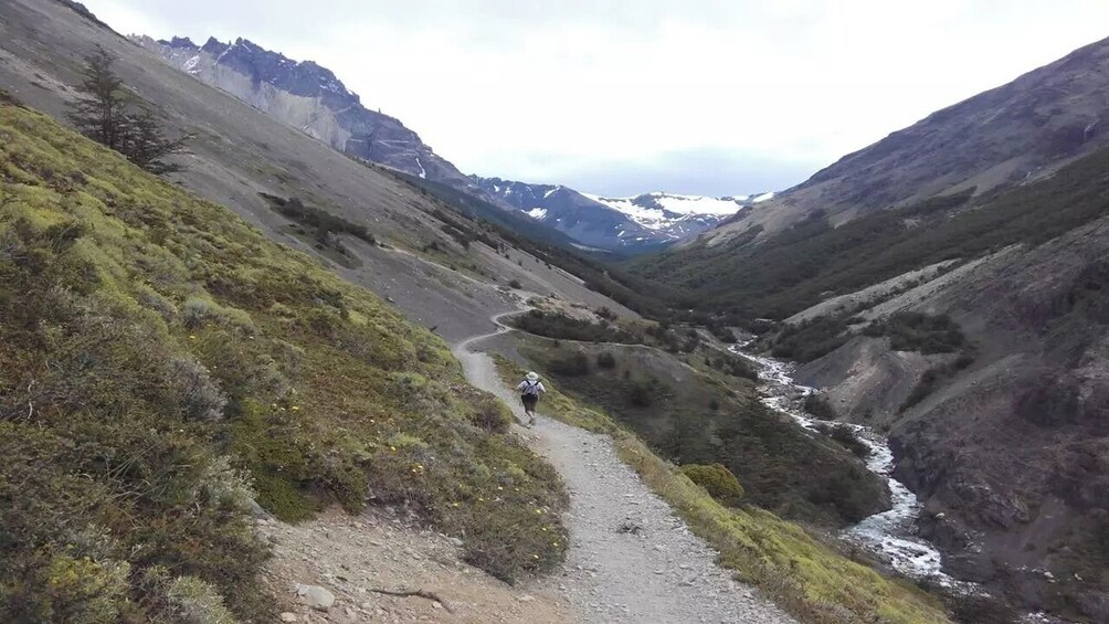A hiker on a narrow mountain trail with a river running through a valley. 4