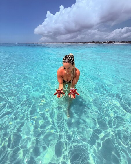 A person in clear turquoise water with a beach and distant buildings in the background. 5