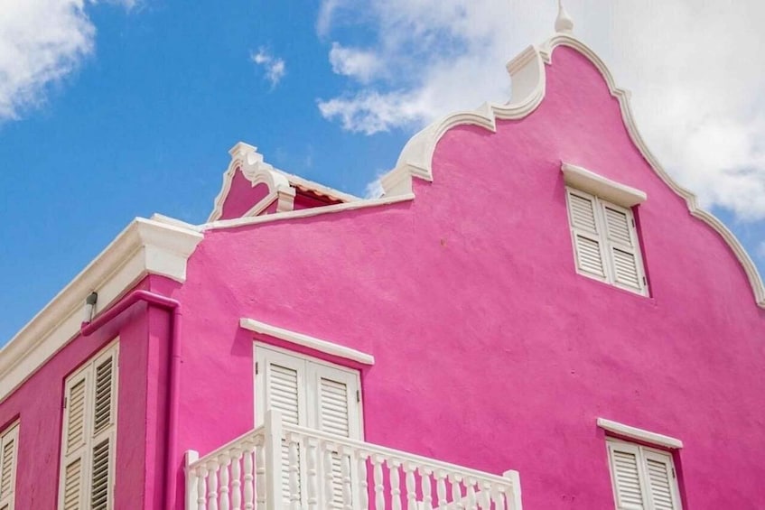 A pink building with white shutters and a balcony. 3