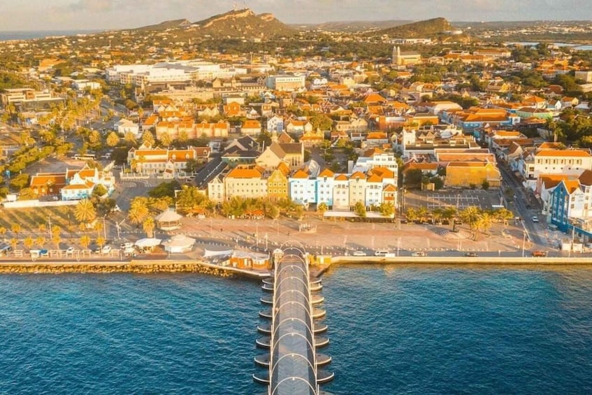An aerial view of a coastal city with a prominent pier extending into the water, surrounded by densely packed buildings and a hilly backdrop. 4