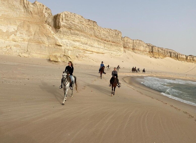 Horseback riders on a sandy beach with cliffs in the background. 2