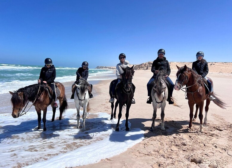 A group of horse riders on a beach with the ocean in the background. 1