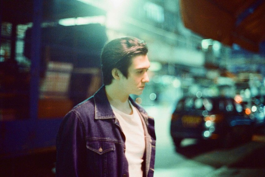 A person standing on a street at night with blurred lights in the background. 1