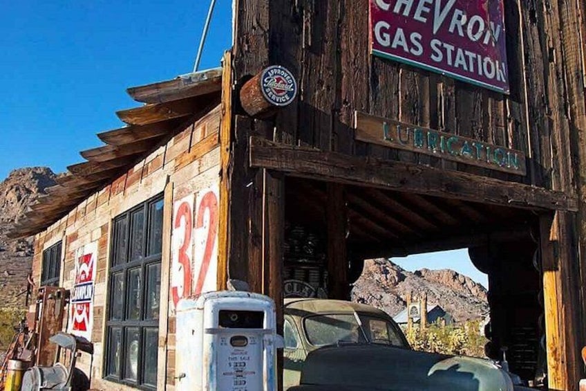 Una antigua estación de servicio Chevron con fachada de madera, una bomba de gasolina y un coche estacionado en la parte delantera. 4