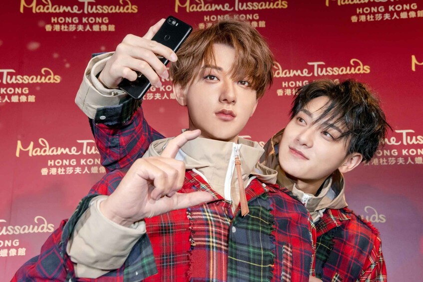 Two individuals in front of a backdrop with text related to Madame Tussauds Hong Kong. 3