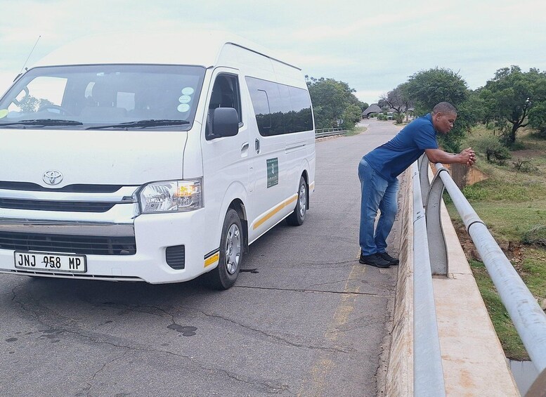 A white Toyota van parked on a road with a man leaning on a metal guardrail. 4