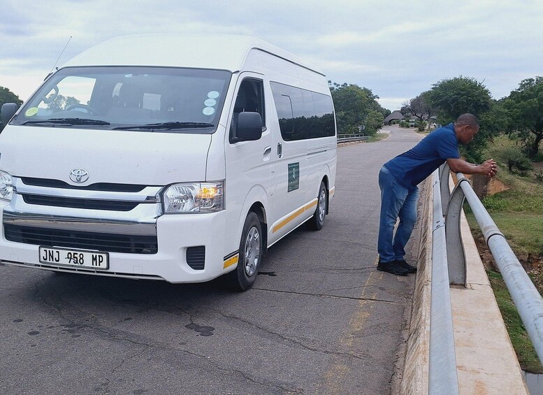 A white Toyota van parked on a road with a man leaning on a guardrail. 2