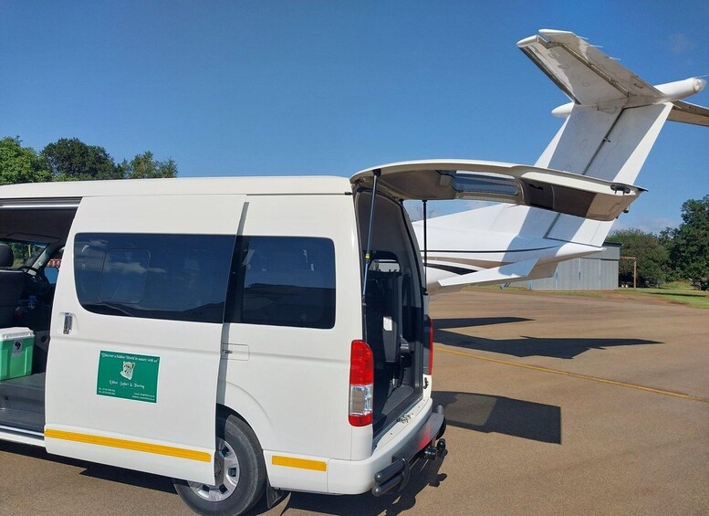 A white van with a green sticker on the side parked next to a large white aircraft with its landing gear extended. 5