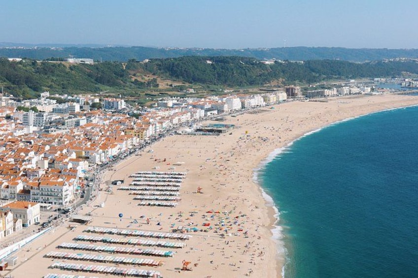 A coastal city with a long beach, rows of beach umbrellas, and buildings along the shore. 5