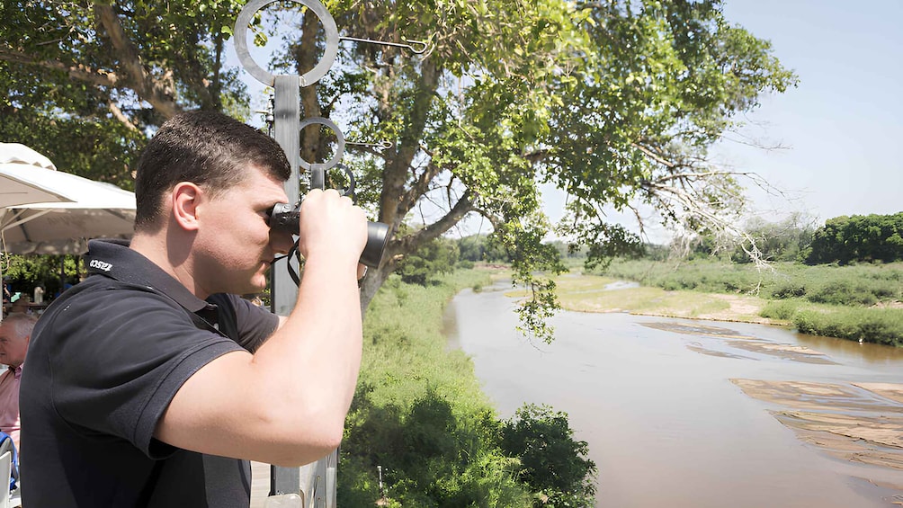 A person using binoculars to observe a river and surrounding greenery. 4