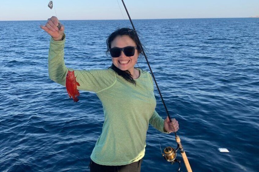 A person holding a fish and a fishing rod over a body of water. 2