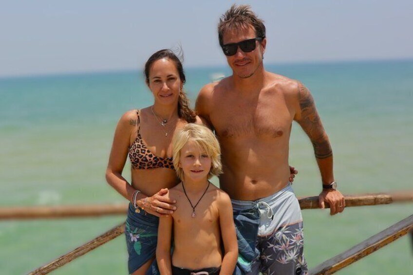 A family on a wooden pier with a beach and ocean in the background. 1