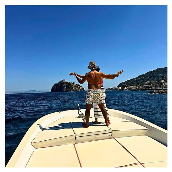 A person standing on a boat facing a coastal landscape with a prominent rock formation. 3