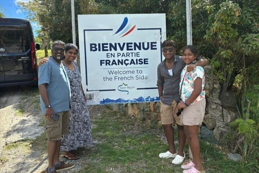 A group of people standing in front of a sign that reads 'BIENVENUE EN PARTIE FRANÇAISE Welcome to the French Side.' 5