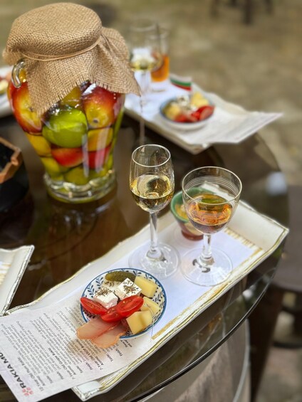 A table with a fruit salad in a jar, two glasses of white wine, and a plate with cheese and tomatoes. 2