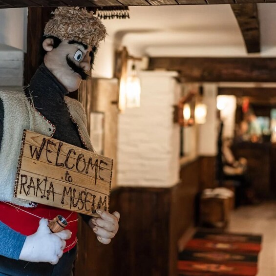 A puppet holding a wooden sign that reads 'WELCOME to RAKIA MUSEUM.' 1