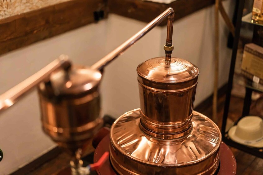 A copper still with a spout and a lid, placed on a wooden surface. 5