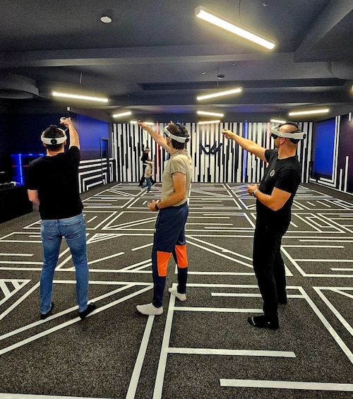 Three people wearing VR headsets in a room with geometric patterns on the floor. 1