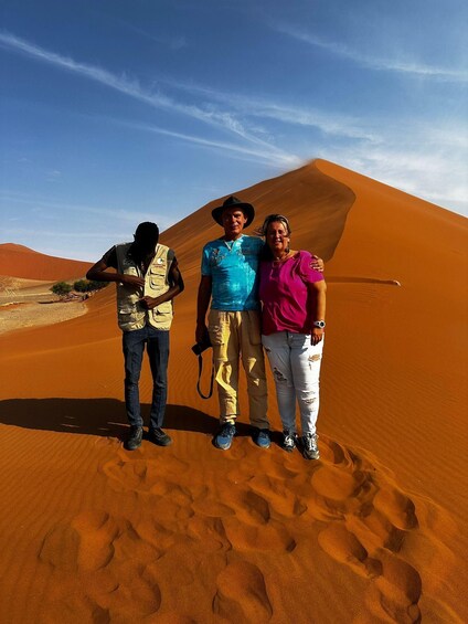 Three people standing on a sand dune with a clear sky in the background. 2