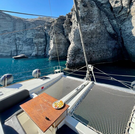 A boat's deck with a table set for a meal, ropes, and a rocky coastline in the background. 4