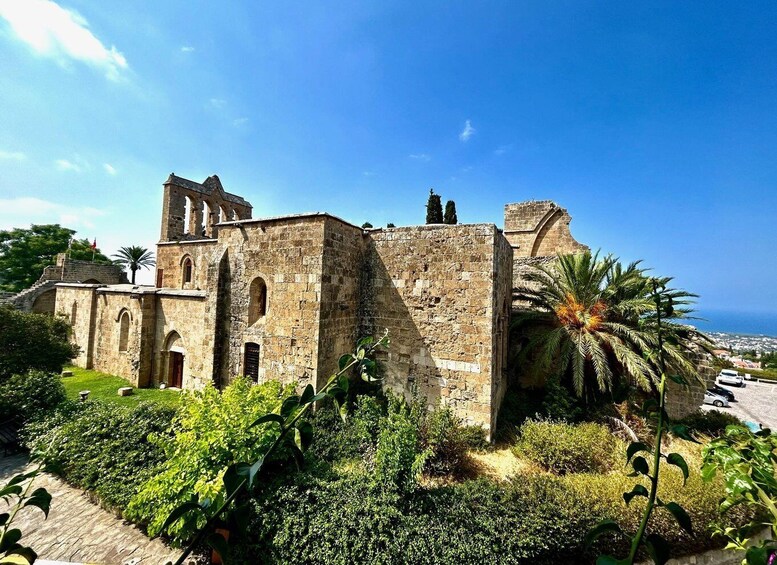A historic stone building with arches and a tower, surrounded by lush greenery and palm trees. 3
