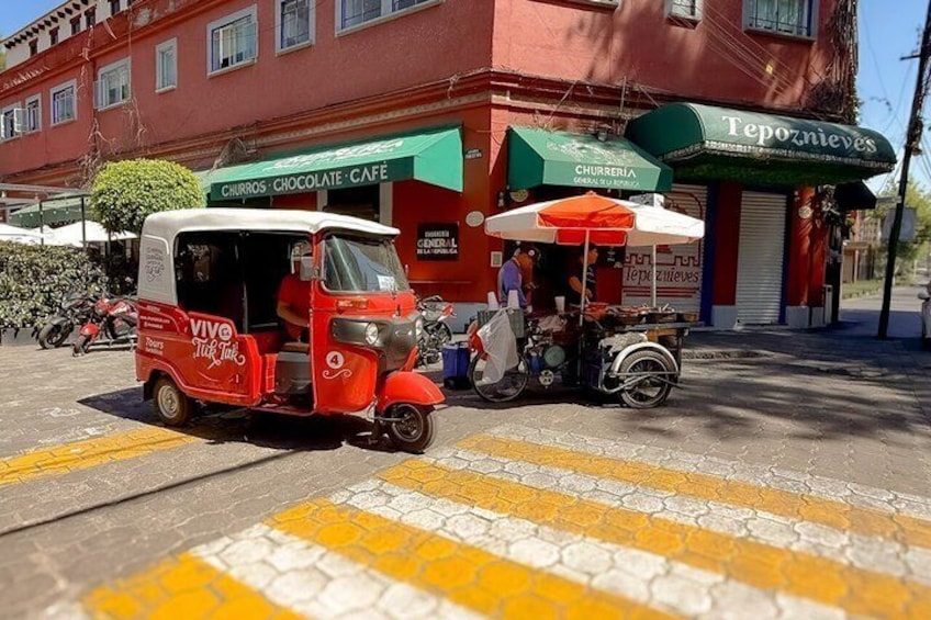 A red auto rickshaw, a street vendor cart, and a building with a green awning. 5