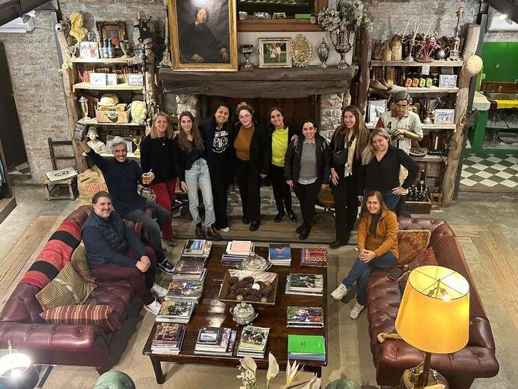A group of people in a cozy, cluttered room with a fireplace, books, and various decorative items. 3