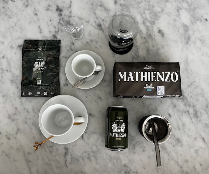 A table with a coffee cup, a glass of water, a bottle of tea, a box of tea, and a tea infuser. 1