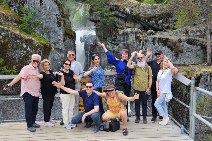 Een groep mensen op een houten platform, met een waterval op de achtergrond. 1