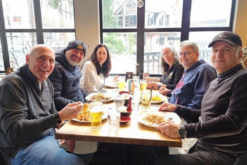 Een groep mensen zit rond een tafel met eten en drinken. 2
