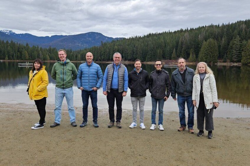 Un groupe de personnes se tient sur une plage de sable au bord d’un lac, avec des montagnes en arrière-plan. 4