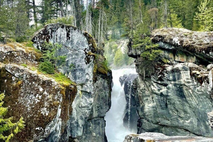 Een waterval stort tussen grote rotsformaties naar beneden in een bebost gebied. 5