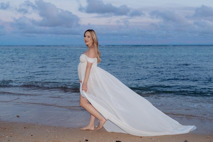 A person in a white dress standing on a beach with a body of water in the background. 5