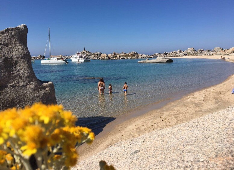 A beach with clear water, a rocky outcrop, and boats in the background. 2