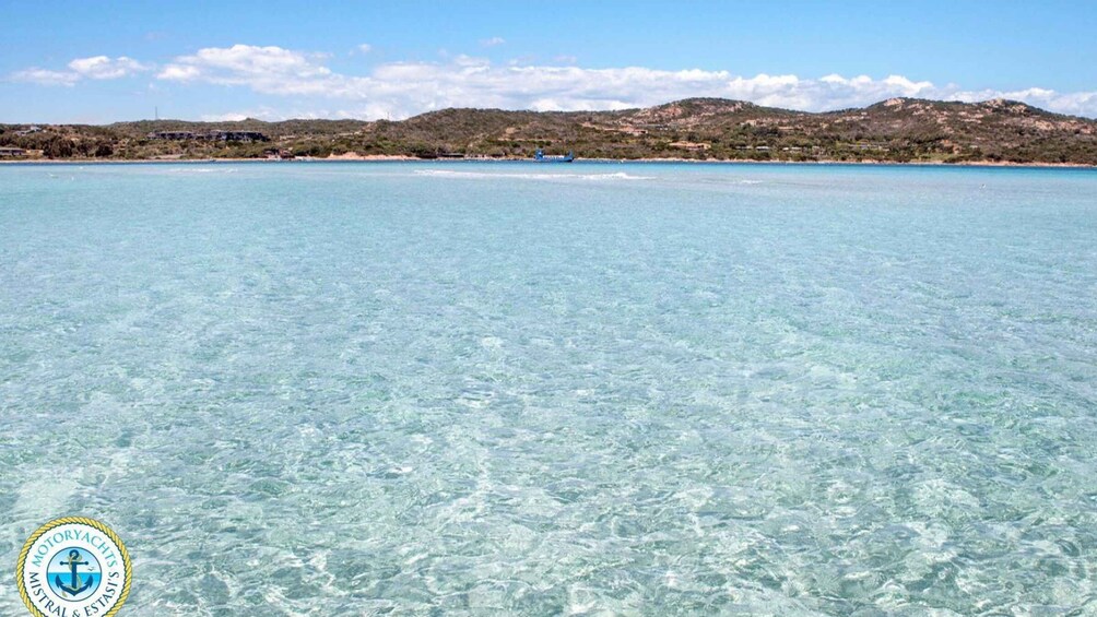 A clear coastal waterway with a distant shoreline, a boat, and a logo in the bottom left corner. 3