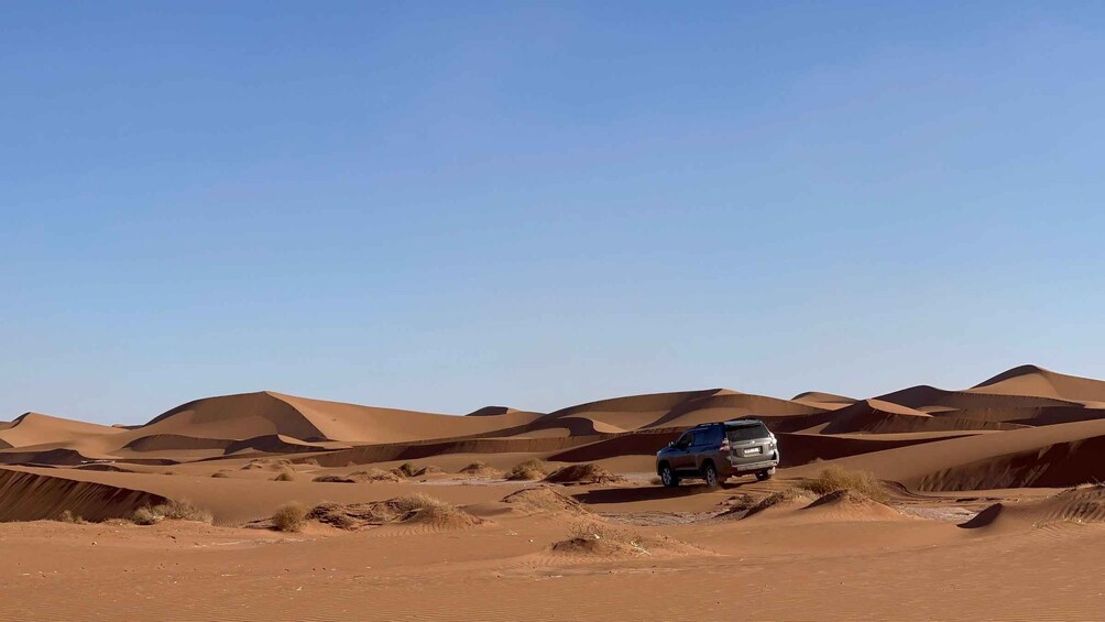 A desert landscape with sand dunes and a vehicle. 1