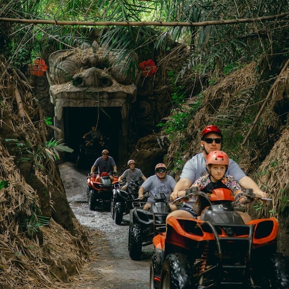 A group of people on ATVs navigating a narrow, muddy path through a dense, tropical forest. 1